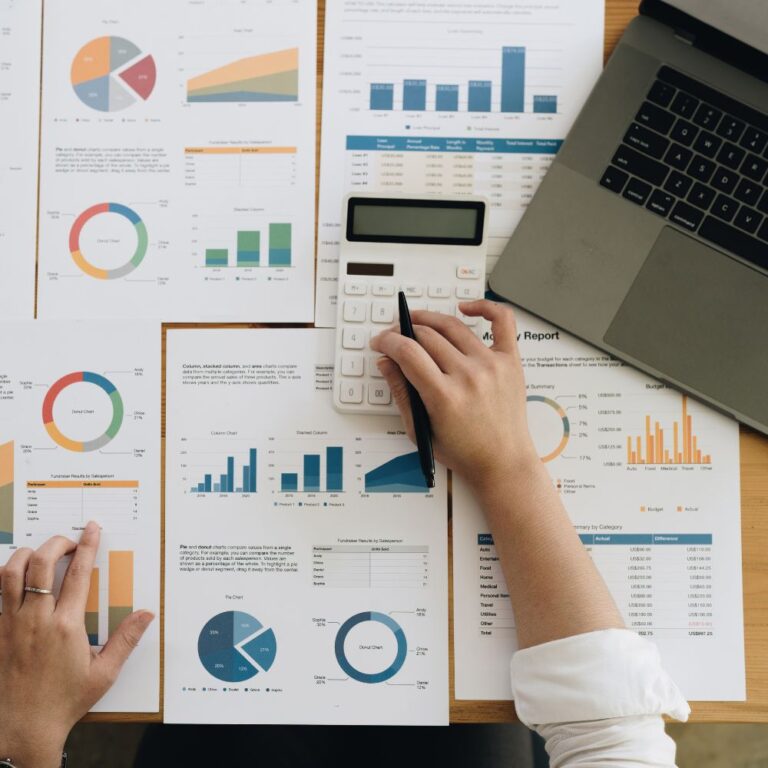 Mehrere Hände zeigen auf Berichte mit Diagrammen am Laptop-Arbeitsplatz