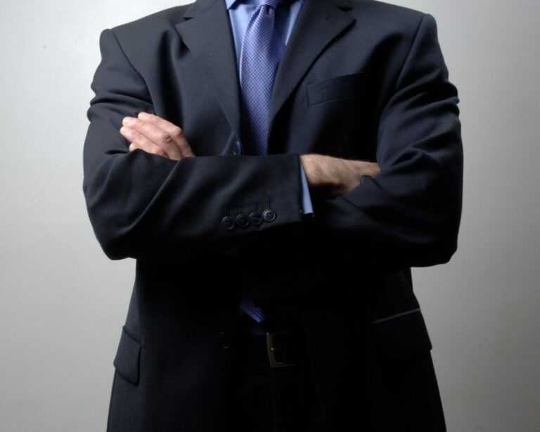 Mann im Anzug mit verschränkten Armen vor neutralem Hintergrund