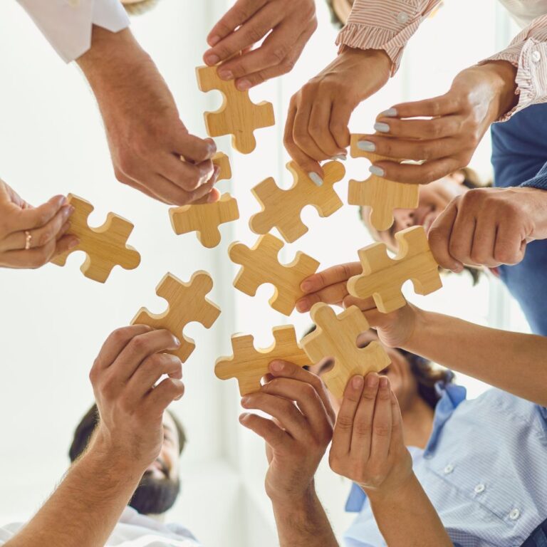Hände mehrerer Personen setzen gemeinsam ein Puzzle zusammen