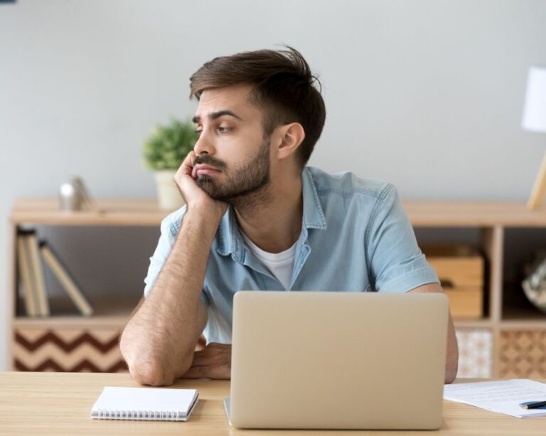 Nachdenklicher Mann sitzt am Schreibtisch mit Laptop und Notizblock