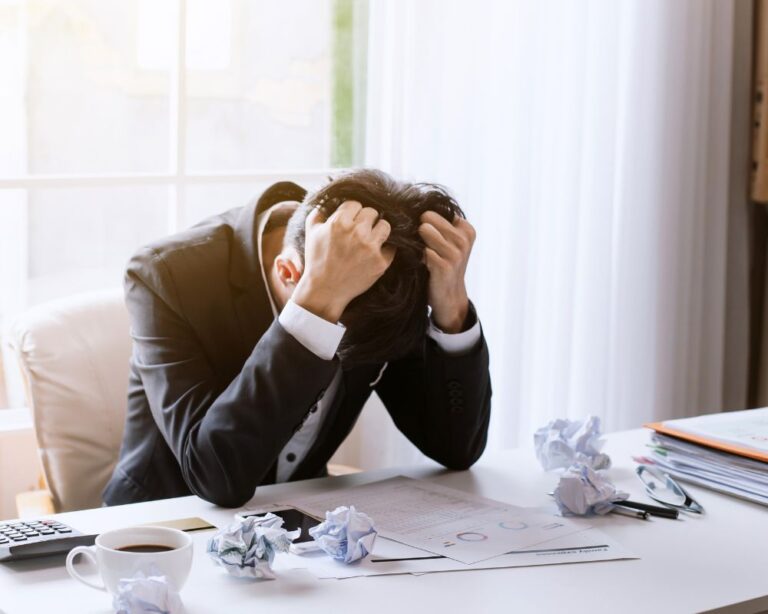 Frustrierter Mann hält den Kopf in den Händen zwischen zerknülltem Papier