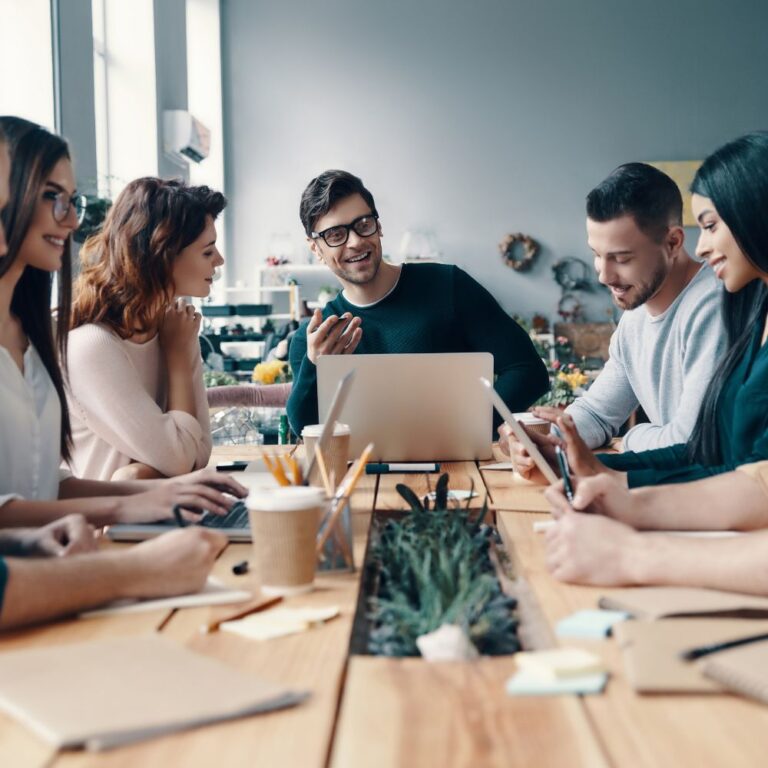 Fröhliches Team arbeitet gemeinsam an einem Konferenztisch mit Laptops