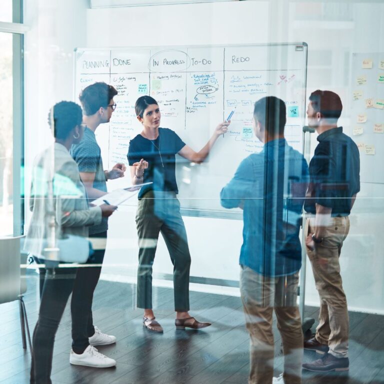 Team steht vor Whiteboard und diskutiert Projektideen