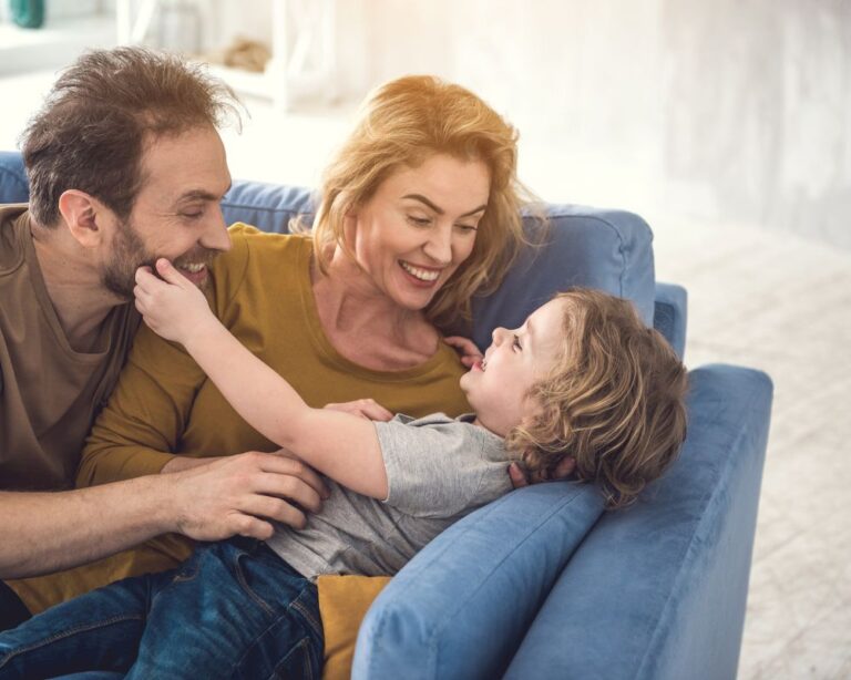 Lachende Familie auf dem Sofa, Eltern spielen mit Kind