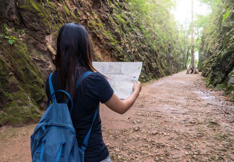 Frau mit Rucksack liest eine Karte auf einem Waldweg
