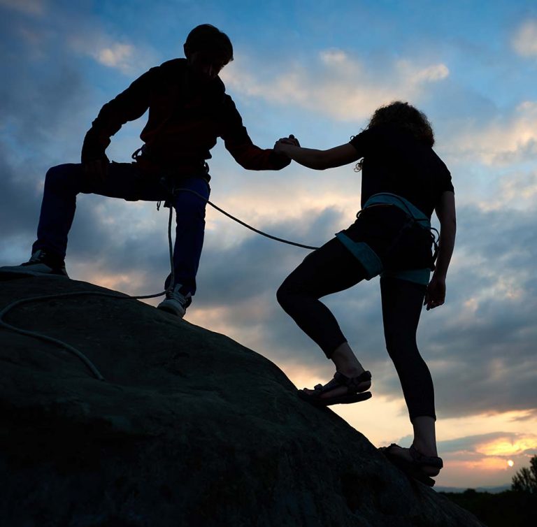 Bergsteiger reicht einem anderen die Hand beim Aufstieg
