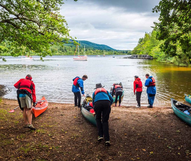 Gruppe von Menschen trägt ein Boot zum Seeufer.